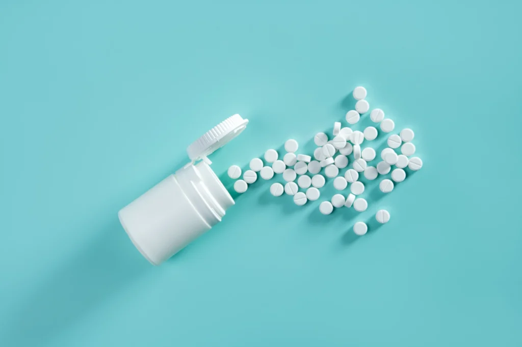 Baclofen Withdrawal Symptoms: A white bottle of pills tipped on its side with white pills spilling across a turquoise background.