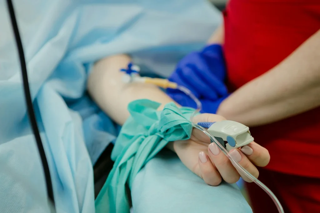 Someone in a hospital bed with an IV and blood oxygen monitor, possibly suffering barbiturate poisoning symptoms.